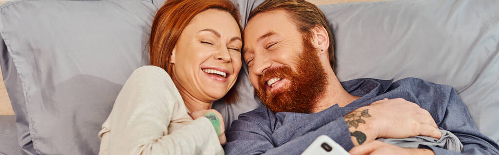 беззаботная рыжая пара проводит время без детей, выходной, веселый муж и жена, бородатый мужчина, улыбающаяся женщина, комфортная жизнь, уютная спальня, смех, баннер  - Фото, изображение