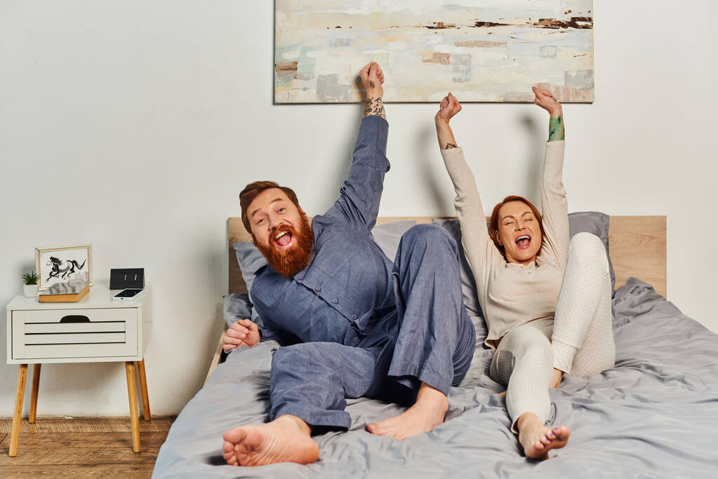 excited people, day off without kids, redhead and happy husband and wife, bearded man and woman with raised hands, parents alone at home, modern lifestyle  - Photo, Image