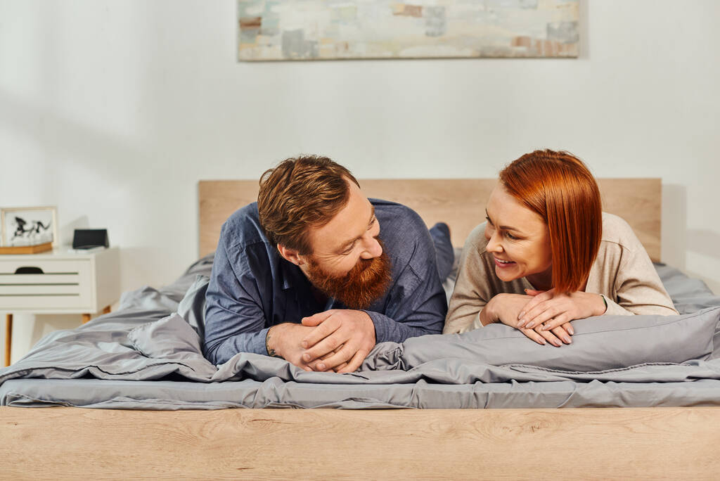 子供がいなくても幸せな夫婦は一緒にリラックスしベッドに横になり赤毛の夫と妻は一緒に楽しい時間を過ごし髭の男と屈託のない女性はお互いを見てタトゥーのある人  - 写真・画像