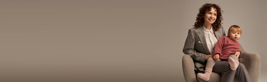 pai trabalhador moderno, equilíbrio trabalho e conceito de vida, mulher encaracolado em terno sentado em poltrona com a filha da criança, fundo cinza, mãe alegre e criança, multitarefa, tempo de qualidade, banner  - Foto, Imagem