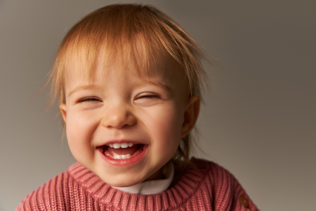 Porträt eines süßen Mädchens, eines fröhlichen Kleinkindes, eines kleinen Kindes in lässiger Kleidung, das im Studio auf grauem Hintergrund in die Kamera blickt, Emotionen, Unschuld, Kleinkindmode, stylisches Outfit, Pullover, Glück  - Foto, Bild