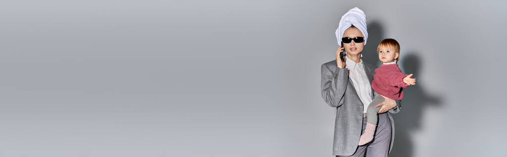 carrière et famille, femme en lunettes de soleil tenant dans les bras fille tout-petit et debout avec serviette sur la tête, mode de vie équilibré, femme d'affaires parlant sur smartphone sur fond gris, bannière  - Photo, image