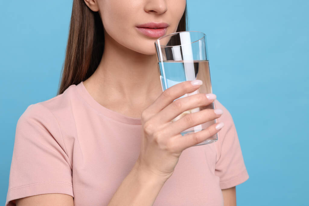 Gesunde Gewohnheit. Frau trinkt Frischwasser aus Glas auf hellblauem Hintergrund, Nahaufnahme - Foto, Bild