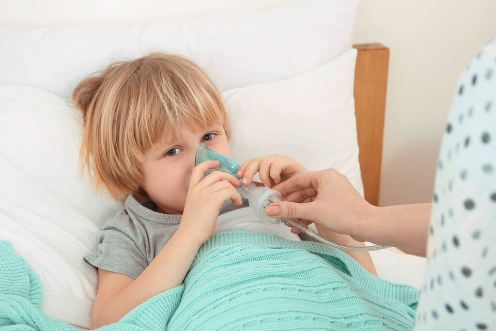 Mother helping her sick son with nebulizer inhalation in bedroom - Photo, Image