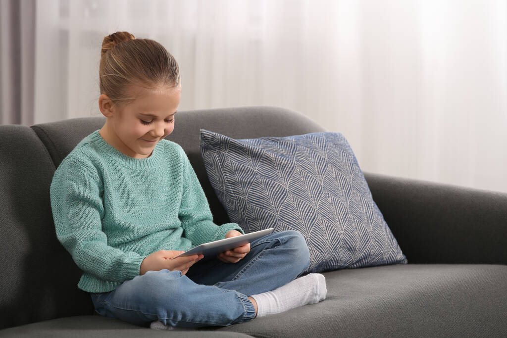 Маленька дівчинка використовує планшет на дивані вдома. Інтернет залежність
 - Фото, зображення