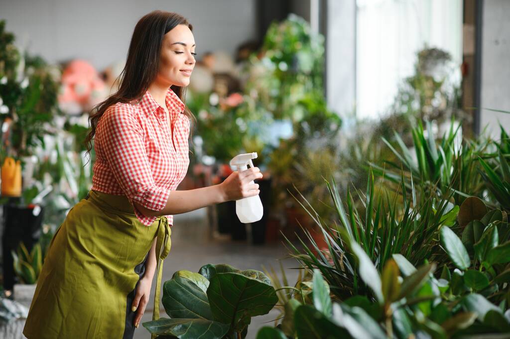 Csinos női kertész vigyáz növények a virágok és növények bolt - nő dolgozik egy üvegházban. - Fotó, kép
