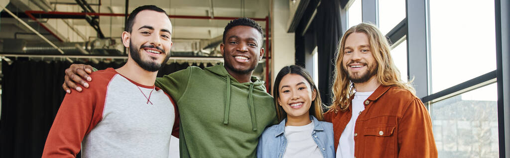mladý a veselý africký Američan objímající stylové a ambiciózní přátele a usmívající se před kamerou v moderní kanceláři, multietnické obchodní partnery, úspěšný start-up, banner - Fotografie, Obrázek