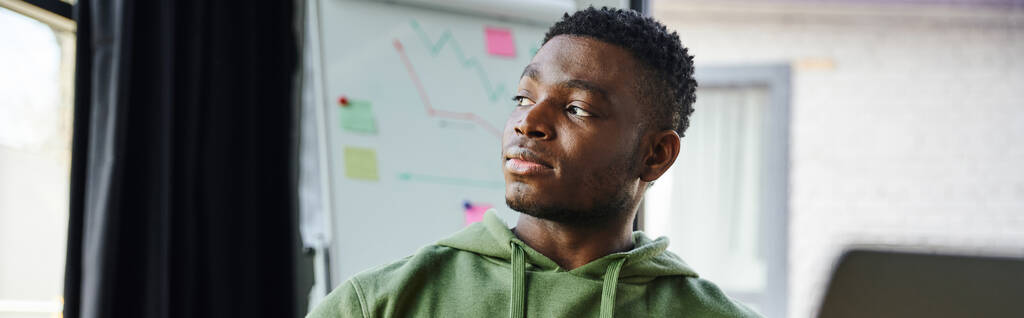 портрет молодого і вдумливого афроамериканського підприємця в зеленому светрі, який дивиться далеко від фліп-чарту з бізнес-аналітикою в сучасному офісі, професійним розвитком, банером
 - Фото, зображення