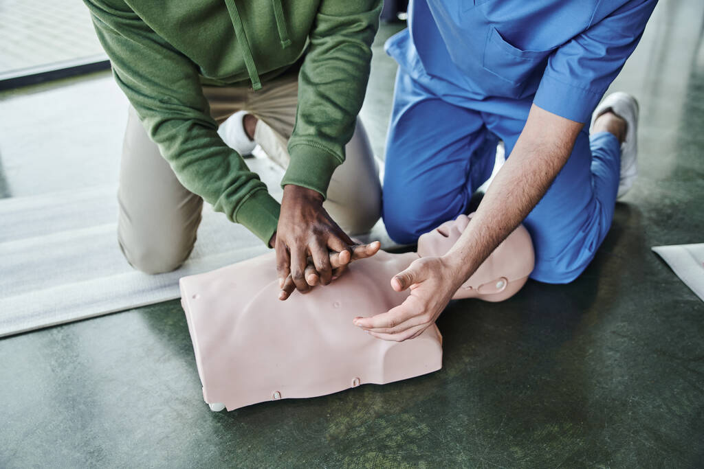 cropped view of african american man practicing life-saving skills and doing chest compressions on CPR manikin near professional paramedic on first aid seminar, emergency preparedness concept, top view - Photo, Image