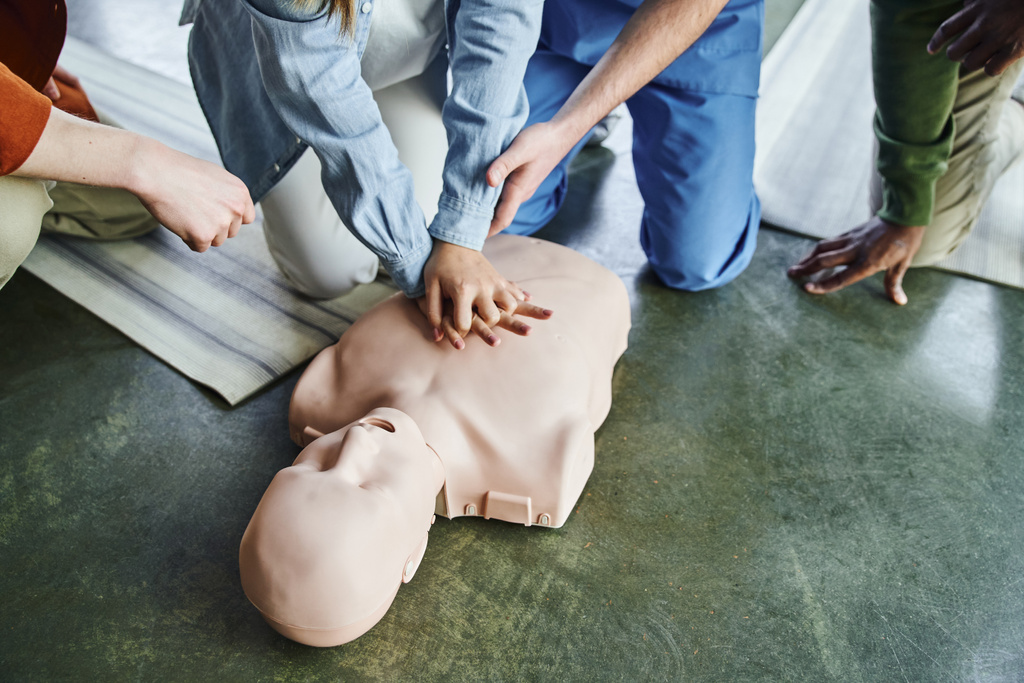 обрізаний погляд на парамедичну допомогу молодої жінки, яка практикує грудні компресії на CPR manikin поблизу багатоетнічних учасників навчального семінару першої допомоги, життєво-зберігаючі навички та концепція методів
 - Фото, зображення