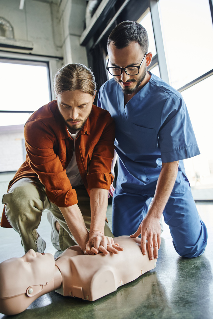 Erste-Hilfe-Kurse, professionelle Sanitäter, die jungen Mann beim Üben von Brustkompressionen an CPR-Schaufensterpuppen unterstützen, effektive lebensrettende Fähigkeiten und Notfallvorsorgekonzept - Foto, Bild