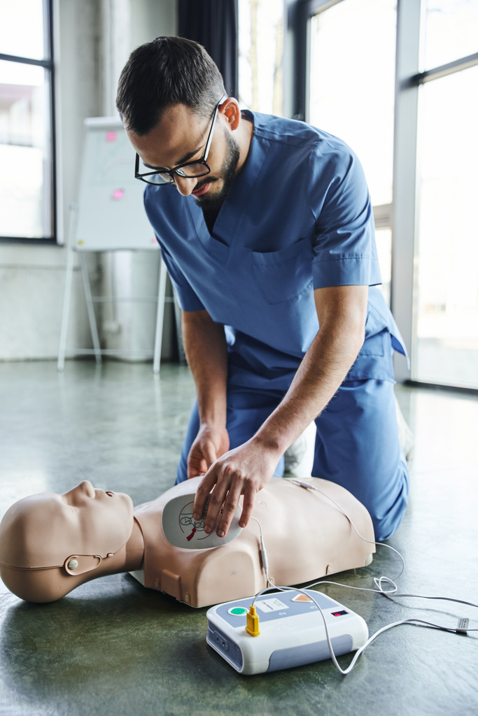 Seminar EHBO-training, jonge medische instructeur in uniform en bril met defibrillator op reanimatiepop, hartreanimatie, gezondheidszorg en levensreddende technieken - Foto, afbeelding