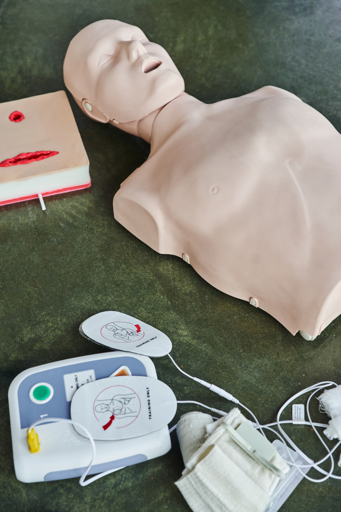 wysoki kąt widzenia manekina CPR w pobliżu symulatora pielęgnacji ran i zautomatyzowanego defibrylatora zewnętrznego na podłodze w sali treningowej, sprzętu medycznego do treningu pierwszej pomocy i rozwoju umiejętności - Zdjęcie, obraz
