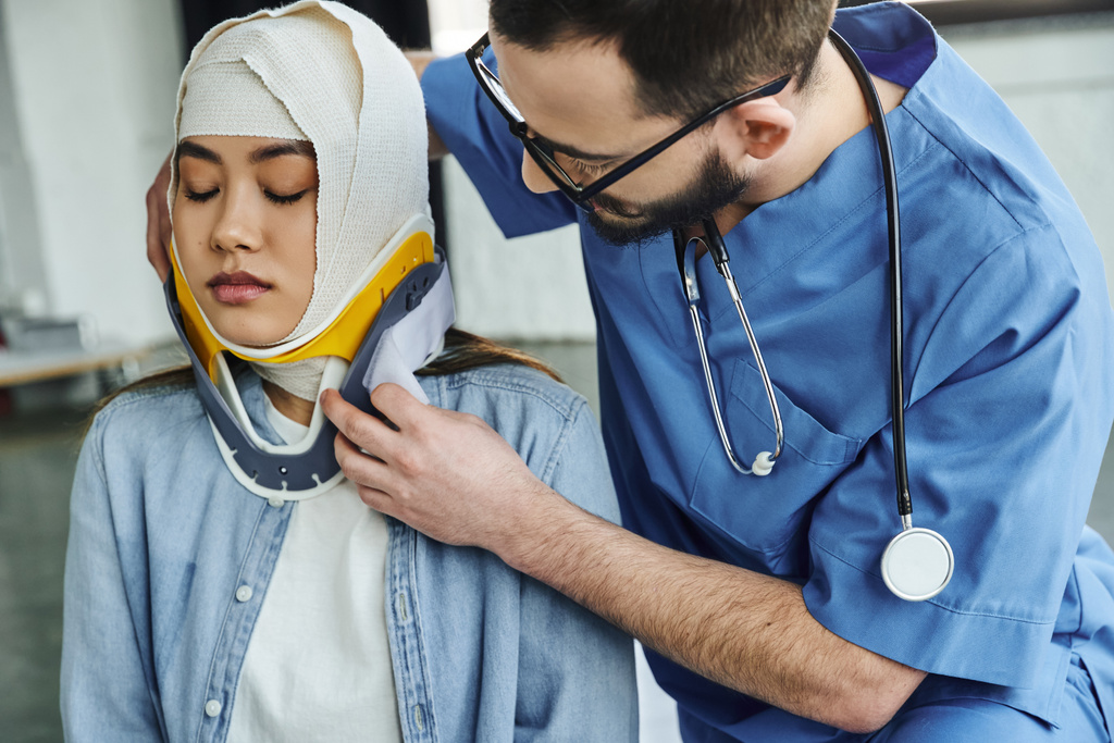 profesionální zdravotník se stetoskopem, v uniformě a brýlích, nasazení krční výztuhy na mladou asijskou ženu s obvázanou hlavou, lékařským výcvikem, koncepcí reakce na první pomoc a nouzové situace - Fotografie, Obrázek