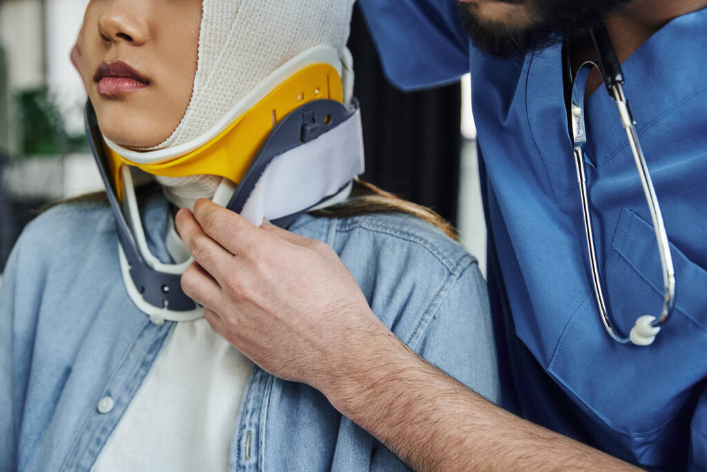 cropped view of professional medical instructor with stethoscope putting neck brace on young woman with bandaged head, first aid and emergency preparedness concept - Photo, Image