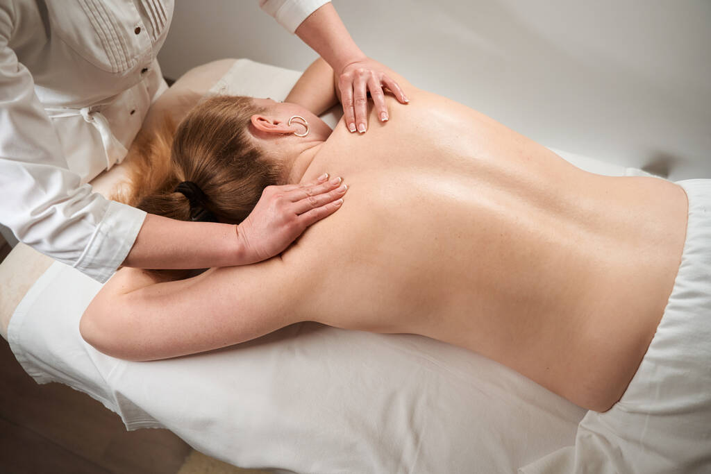 Masseuse female makes manual massage to blonde woman, woman with a bare back lies on a massage table - Photo, Image