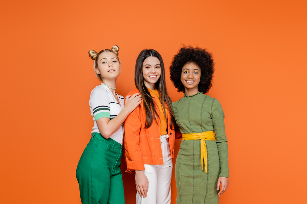 Группа межрасовых моделей подростков в стильном наряде позируют и улыбаются в камеру, стоя вместе на оранжевом фоне, модное поколение z концепции, дружбы и товарищества - Фото, изображение