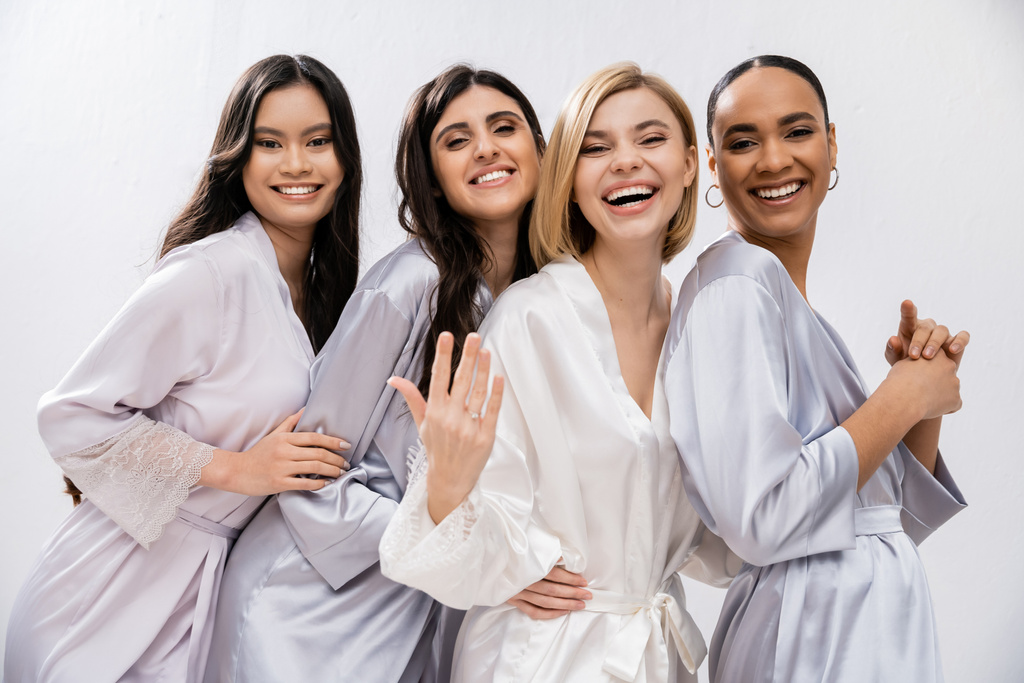 menyasszony zuhany, négy nő, boldog menyasszony mutatja eljegyzési gyűrű közelében fajok koszorúslányok selyem köntösben, kulturális sokszínűség, szórakozás együtt, barátság célokat, barna és szőke nők  - Fotó, kép