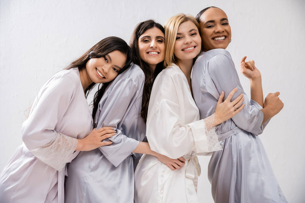 ducha nupcial, cuatro mujeres, novia feliz y damas de honor en túnicas de seda, mirando a la cámara, diversidad cultural, divertirse juntos, objetivos de amistad, morena y mujeres rubias  - Foto, imagen