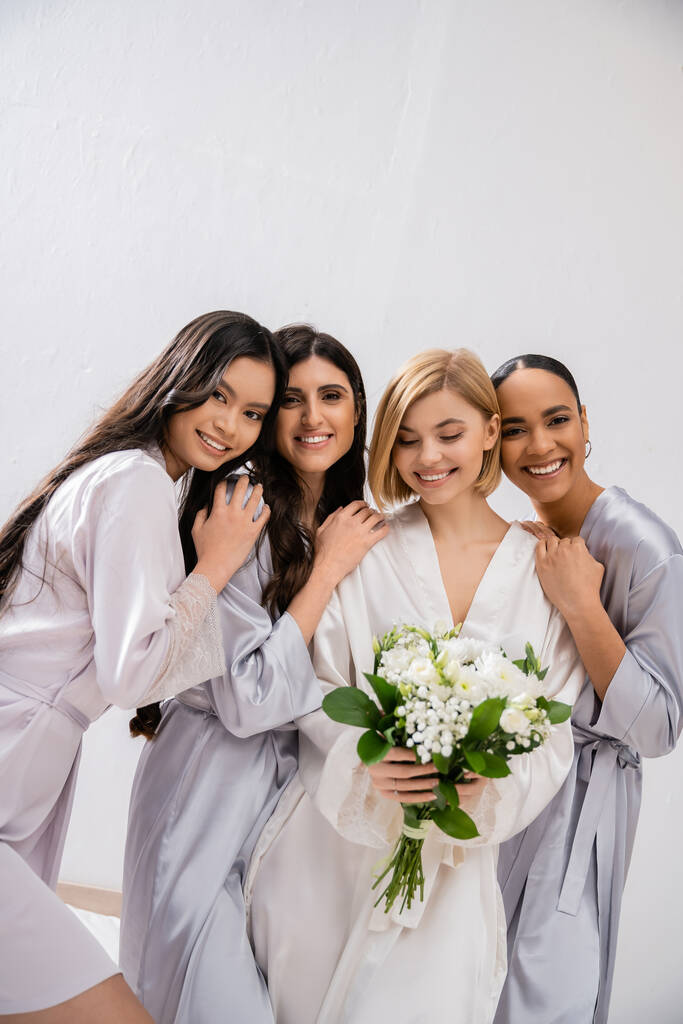 impreza ślubna, cztery kobiety, radosna panna młoda trzymająca bukiet z białymi kwiatami w pobliżu druhen w jedwabnych szatach, różnorodność kulturowa, wspólnota, cele przyjaźni, brunetki i blondynki  - Zdjęcie, obraz