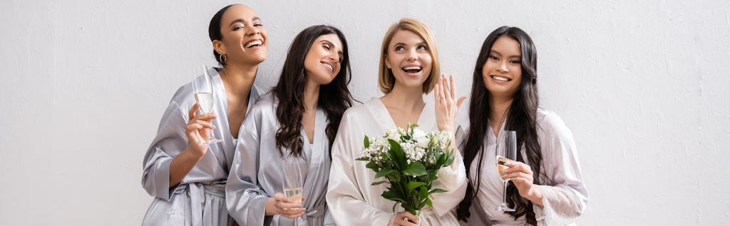 Brautparty, multikulturelle Frauen mit Gläsern mit Champagner, Braut mit weißen Blumen, die ihren Verlobungsring zeigt, Brautjungfern, Vielfalt, Positivität, Brautstrauß, grauer Hintergrund, Banner - Foto, Bild