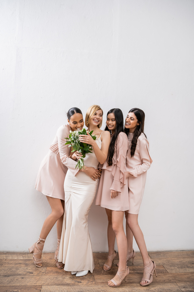 vzrušení, šťastné multikulturní družičky objímající nevěstu ve svatebních šatech, svatební kytice, šedé pozadí, rasová rozmanitost, móda, brunetky a blondýna, skupina žen, bílé květy  - Fotografie, Obrázek