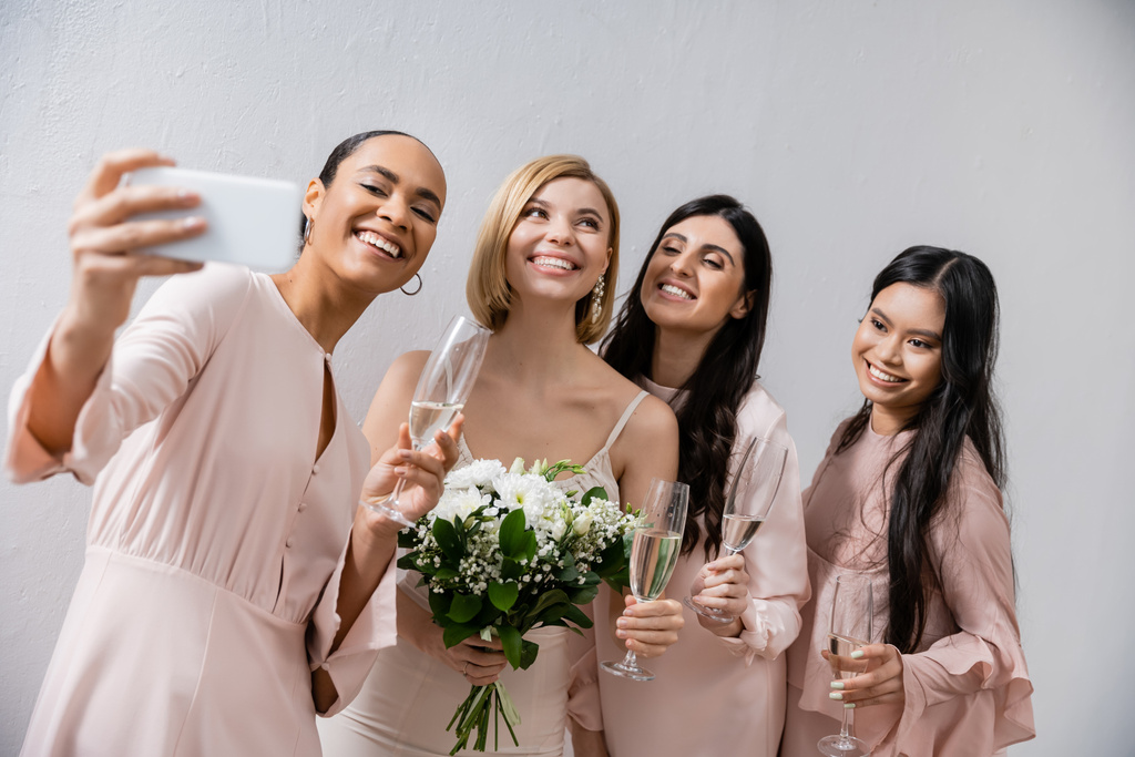 τέσσερις γυναίκες, χαρούμενη νύφη και οι πολυπολιτισμικές παράνυφες της βγάζουν selfie μαζί, ευτυχία, ποτήρια σαμπάνιας, νυφικό μπουκέτο, νυφικό φόρεμα, μελαχρινές και ξανθές γυναίκες  - Φωτογραφία, εικόνα