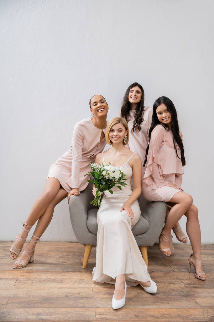 wedding photography, happy four women, bride and bridesmaids, interracial girlfriends, wedding day, cultural diversity, sitting on armchair, grey background, happiness and joy, bridal gown  - Photo, Image