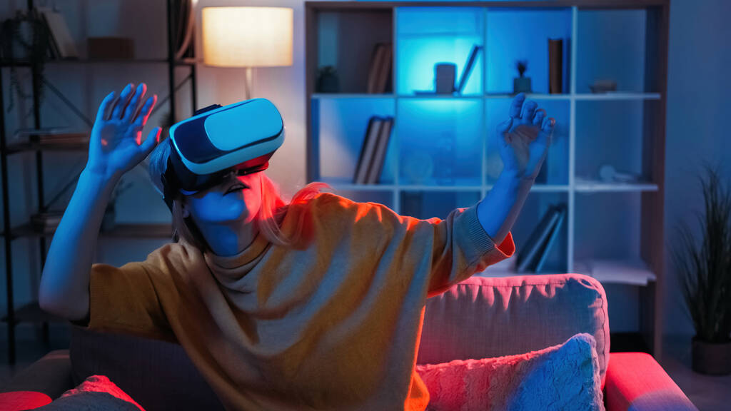 Gra wirtualna. Kobiecy gracz. Technologia VR. Wstrząśnięta kobieta w goglach patrząc zaskoczony gry cyber w ciemnym neon światła wnętrza domu. - Zdjęcie, obraz