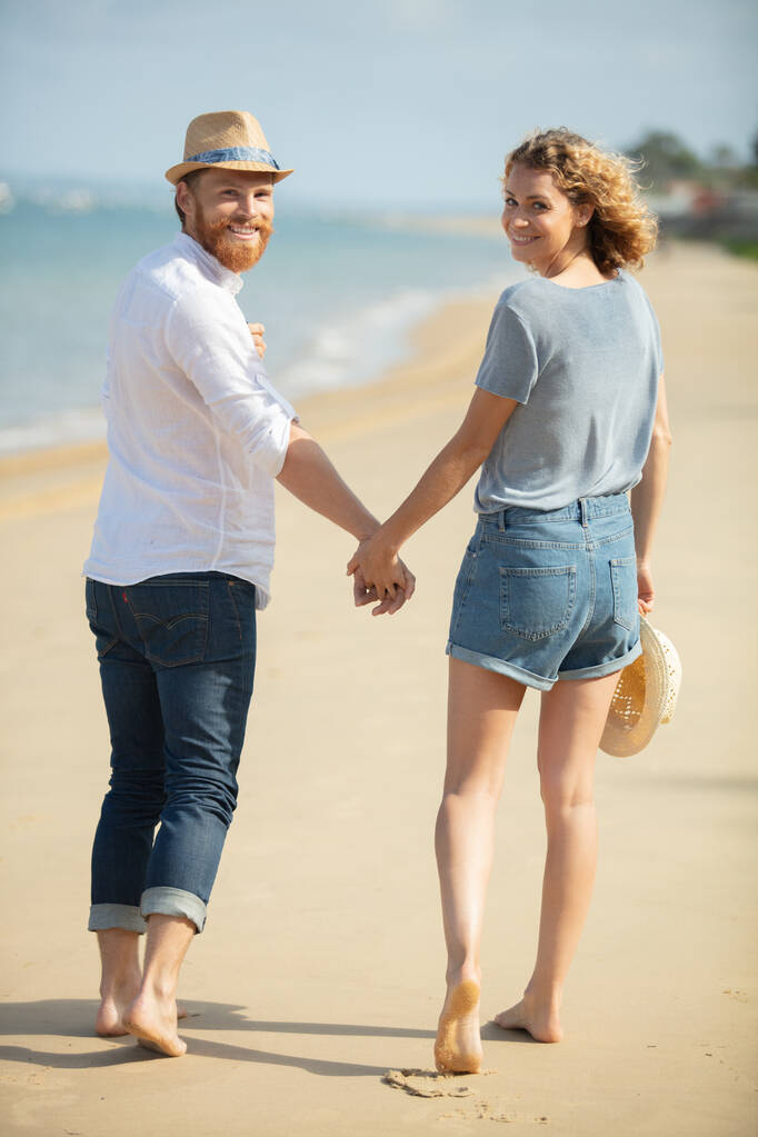 paar wandelen hand in hand langs het strand - Foto, afbeelding