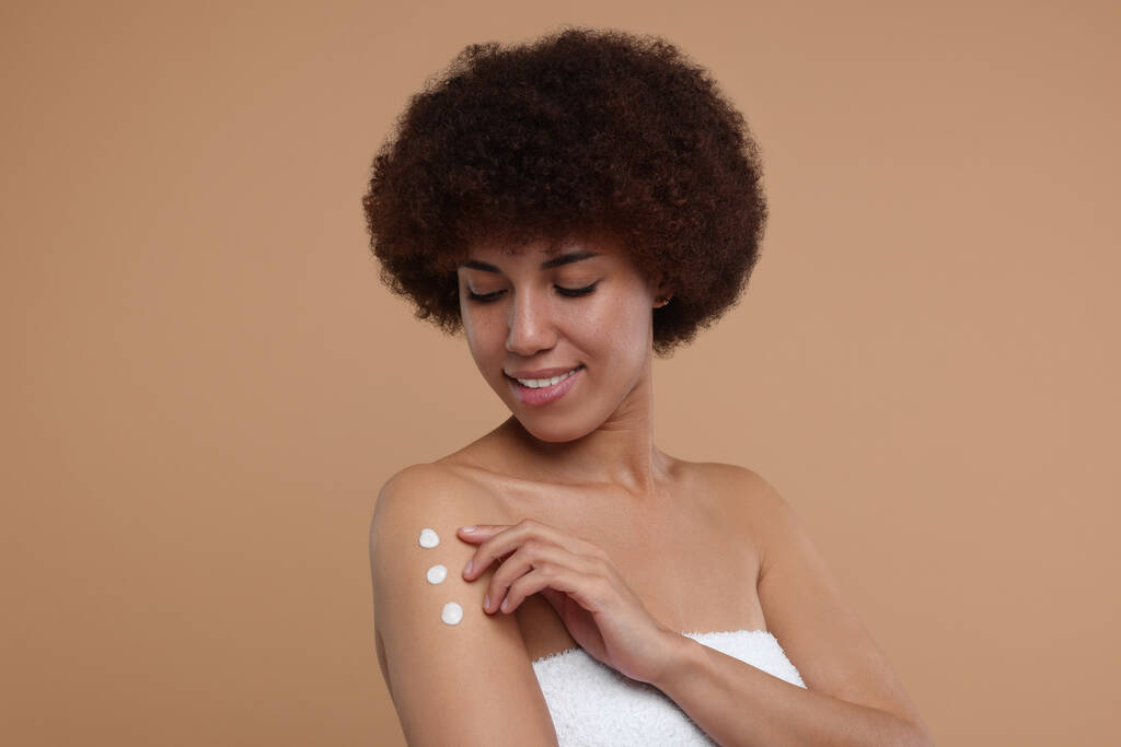 Krásná mladá žena použití tělo krém na paži na béžovém pozadí - Fotografie, Obrázek
