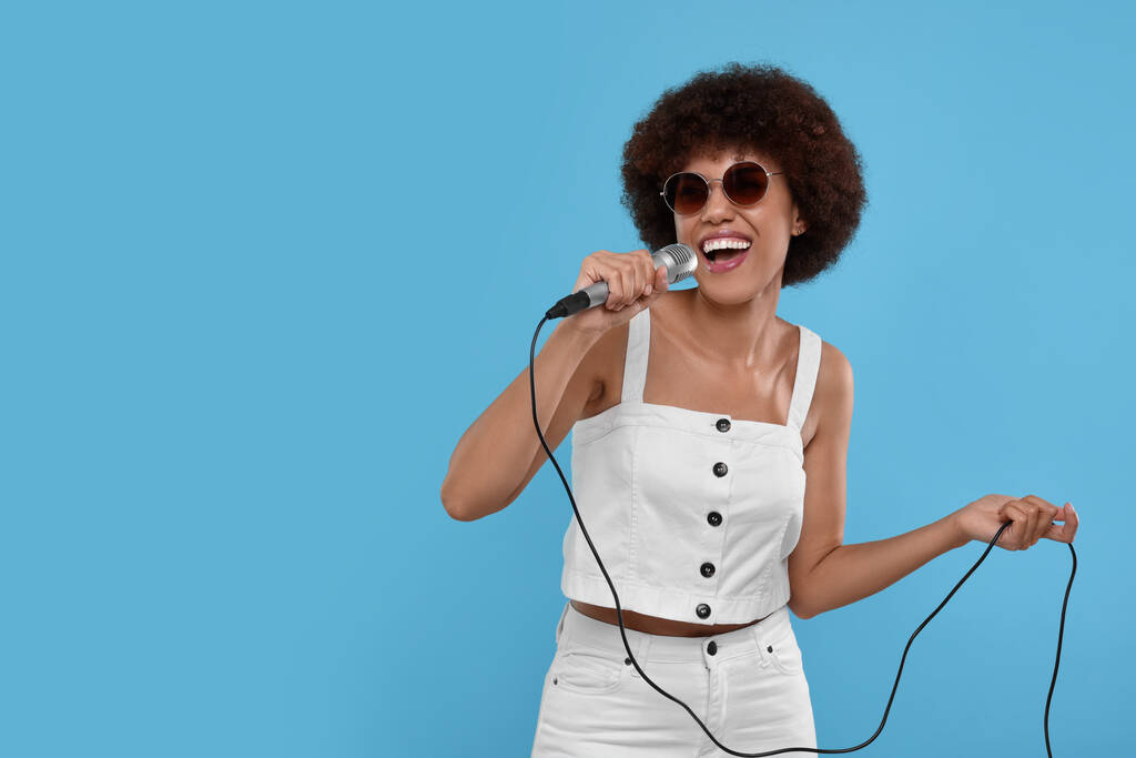 Mujer joven rizada con micrófono cantando sobre fondo azul claro, espacio para texto - Foto, imagen
