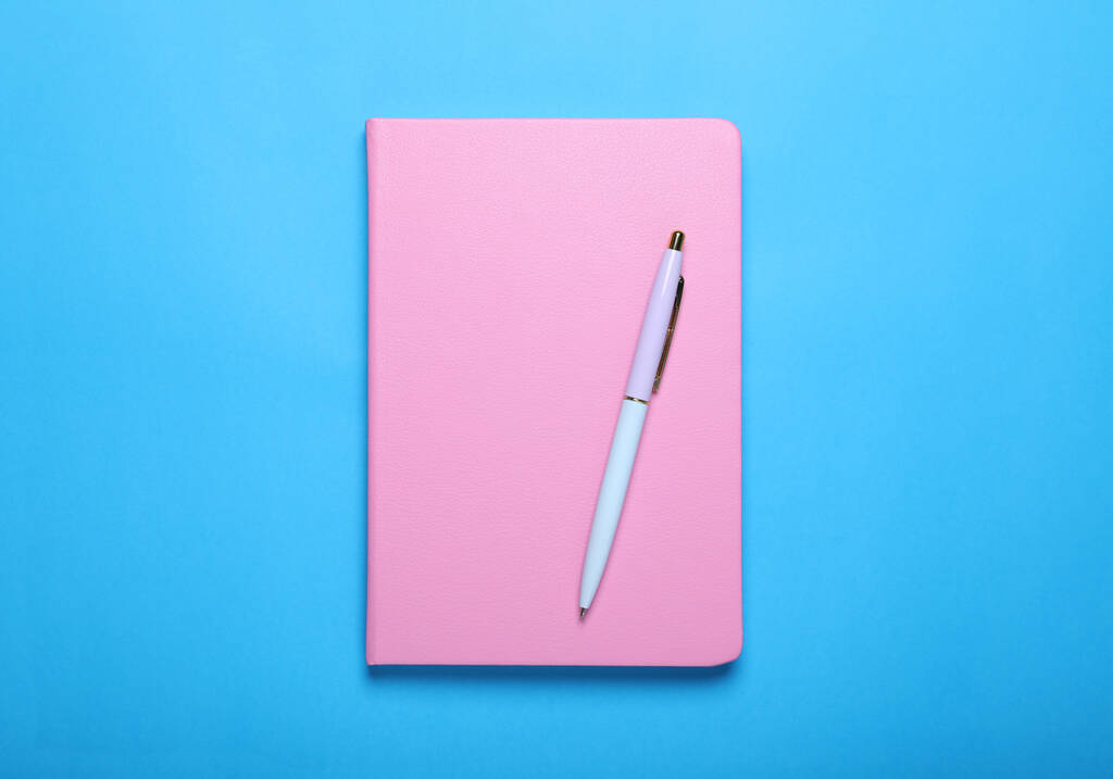 Закритий рожевий блокнот і ручка на світло-блакитному фоні, вид зверху
 - Фото, зображення
