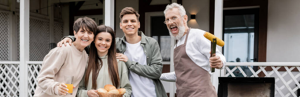 family photo, happy parents day, cheerful middle aged parents having bbq party with teenage daughter and young adult son, excited father holding tongs with grilled corn, looking at camera, banner - Photo, Image