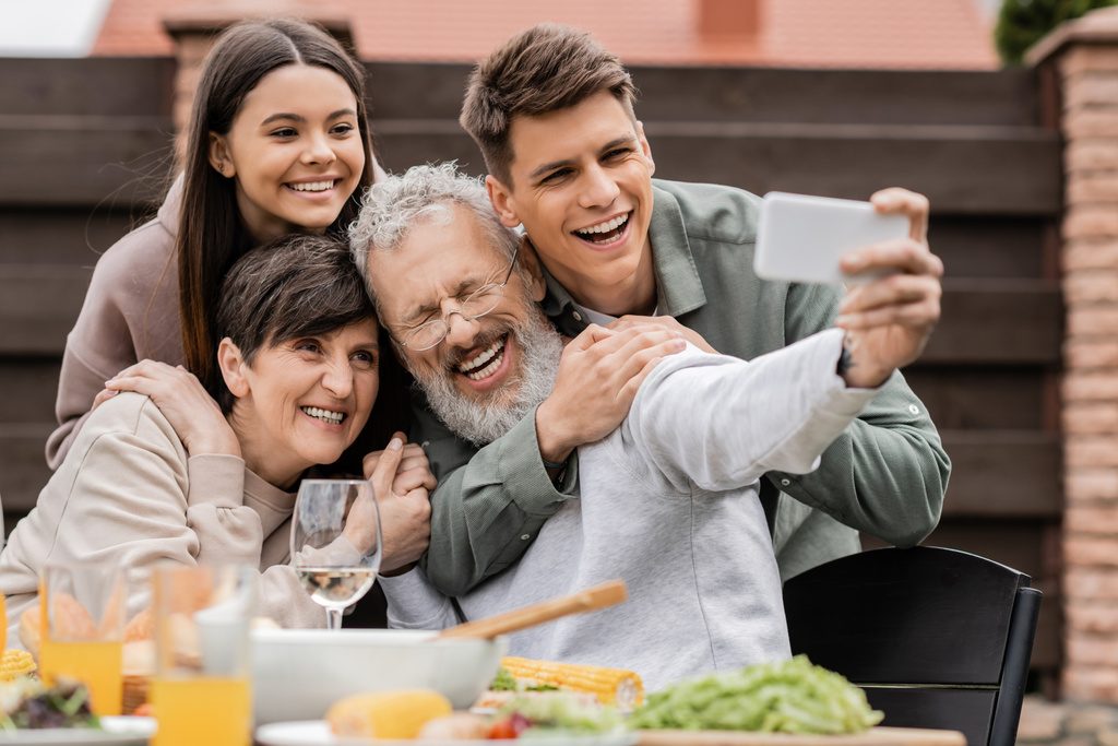 Veselé děti objímající rodiče středního věku, zatímco se selfie na smartphone spolu během grilování párty a rodiče den oslav na dvorku v červnu, šťastný rodiče den koncept - Fotografie, Obrázek