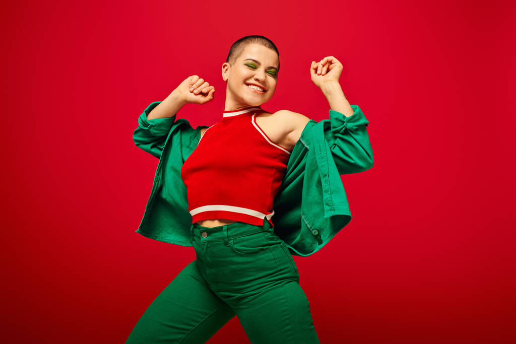 youth culture, stylish appearance, bold makeup, happy and tattooed, short haired woman in green outfit dancing on red background, generation z, youth, vibrant backdrop, individuality, personal style  - Photo, Image