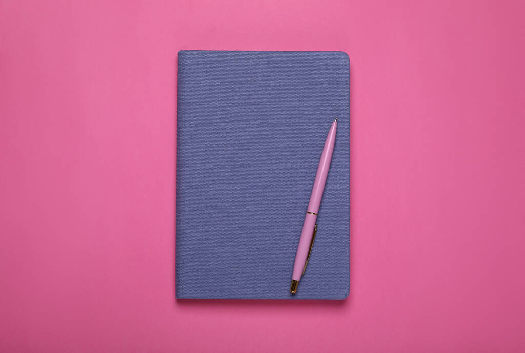 Niebieski notatnik biurowy i długopis na różowym tle, widok z góry - Zdjęcie, obraz