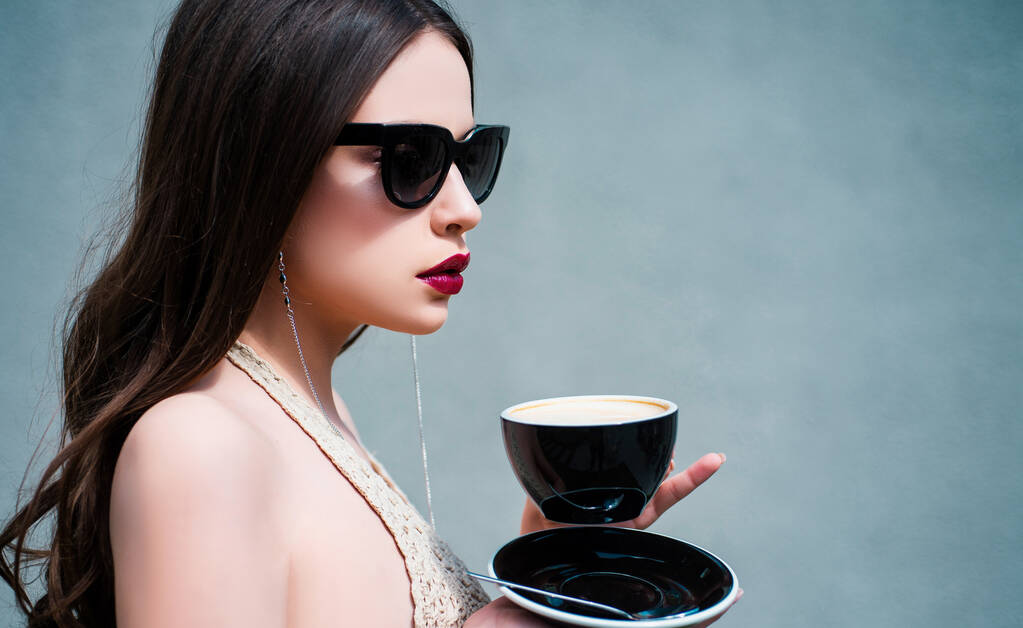 Morning coffee. Beautiful fashion model posing in glasses. Beauty trends. Female fashion model posing with cup. Young woman posing. Portrait of serious woman in the grey isolated - Photo, Image