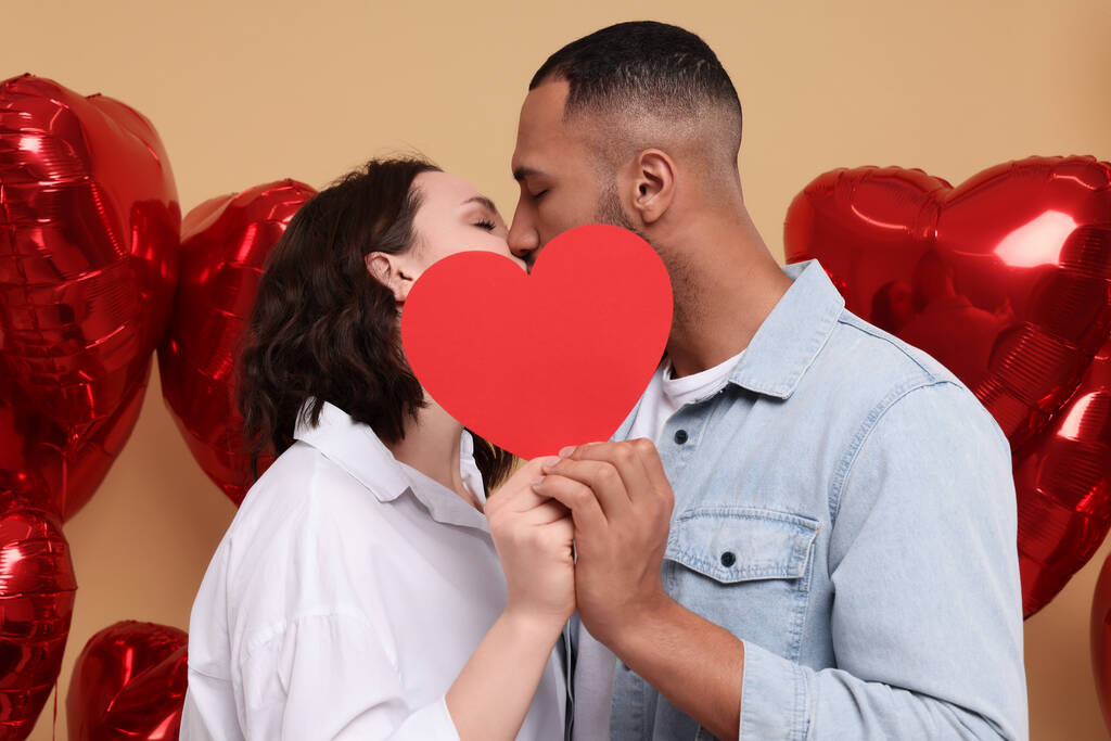 Ihana pari suutelee punaisen paperin sydämen takana beige taustalla. Ystävänpäivän juhla - Valokuva, kuva