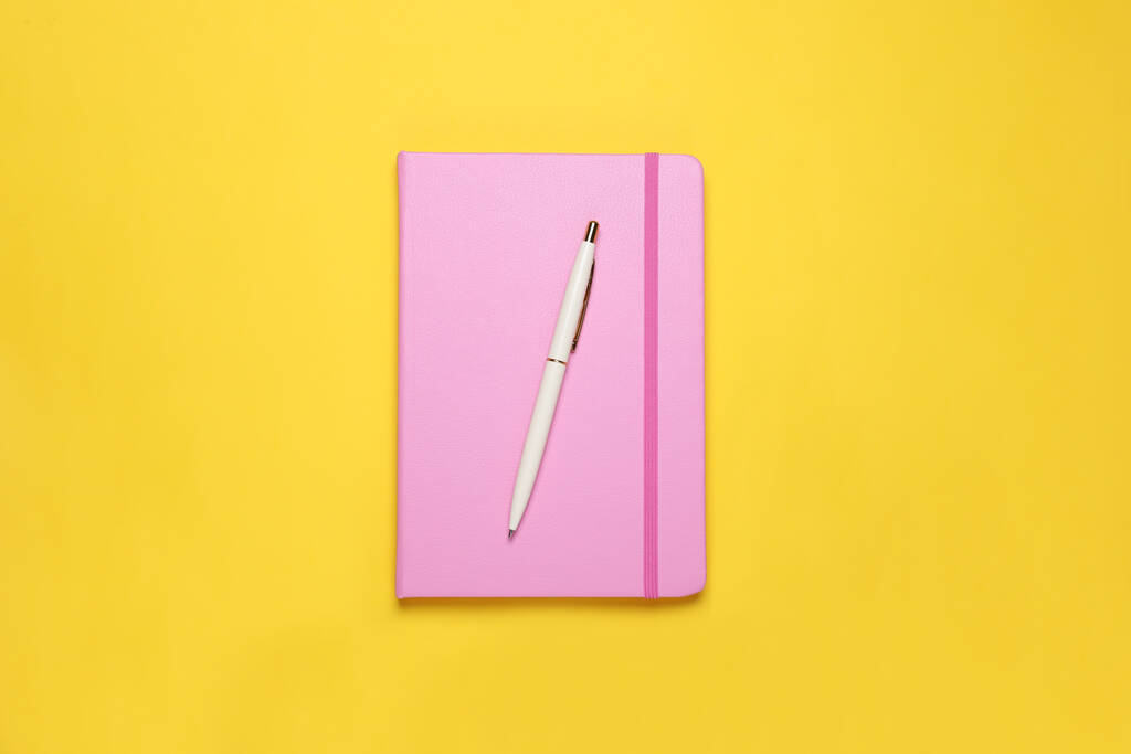 Gesloten roze notitieboekje en pen op gele achtergrond, bovenaanzicht - Foto, afbeelding