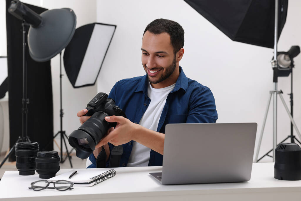 Молодий професійний фотограф з фотоапаратом за столом у сучасній фотостудії
 - Фото, зображення