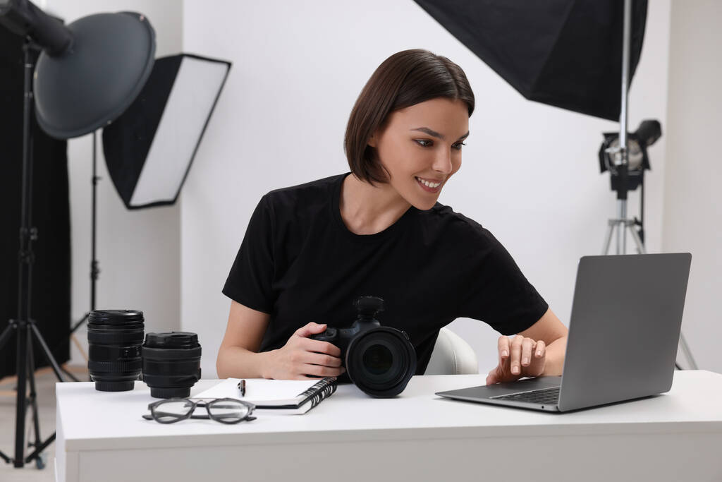 Jonge professionele fotograaf met camera aan het werk op laptop in moderne fotostudio - Foto, afbeelding