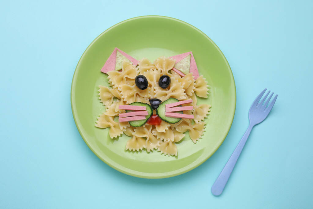 Creatief serveren voor kinderen. Bord met schattige kat gemaakt van lekkere pasta, groenten en worst op lichtblauwe achtergrond, plat gelegd - Foto, afbeelding