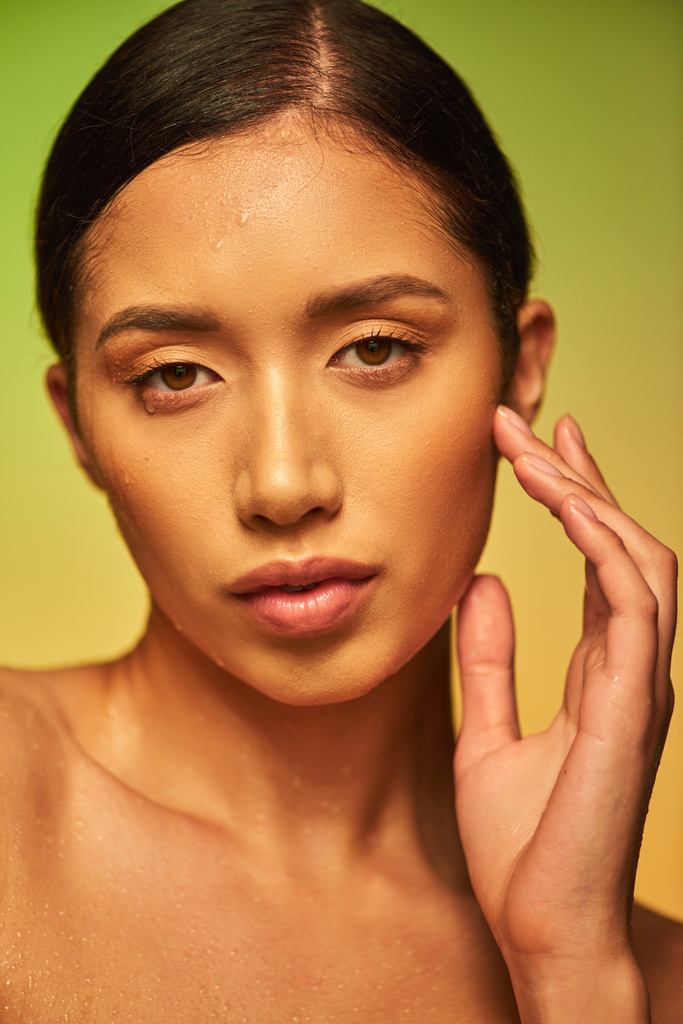 Wassertropfen, Nahaufnahme einer jungen asiatischen Frau mit feuchter Haut, die in die Kamera auf grünem Hintergrund blickt, Hautfeuchtigkeit, braune Augen, Schönheitskampagne, Perfektion, Wohlbefinden, konzeptionelle  - Foto, Bild