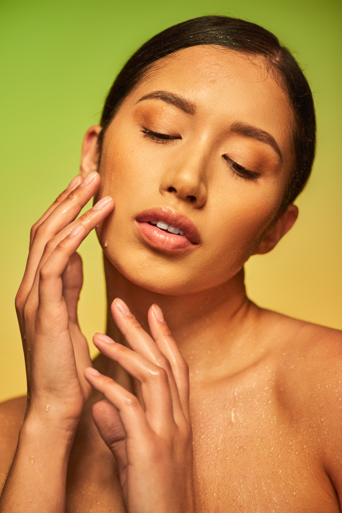 water druppels op het gezicht, close-up van jonge Aziatische vrouw met natte huid aanraken gezicht op groene achtergrond, gesloten ogen, hydratatie van de huid, schoonheid campagne, perfectie, wellness, conceptuele  - Foto, afbeelding