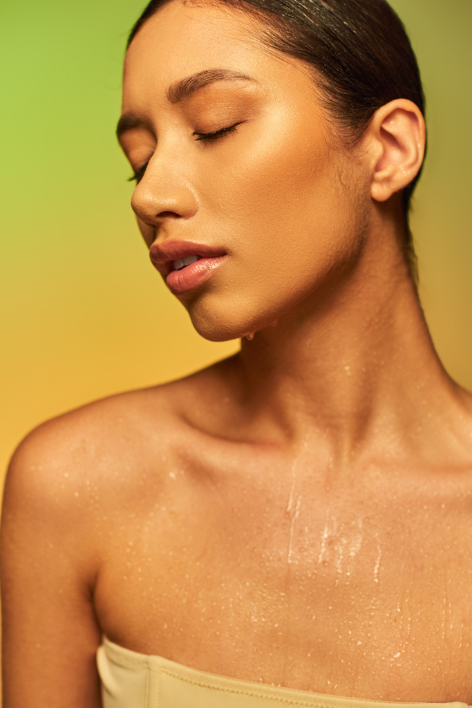 Flüssigkeitszufuhr, junge asiatische Frau mit nackten Schultern und nassem Körper posiert auf einem grünen Hintergrund, geschlossenen Augen, Hautpflege-Kampagne, Schönheitsmodel, brünettes Haar, glühende Haut  - Foto, Bild
