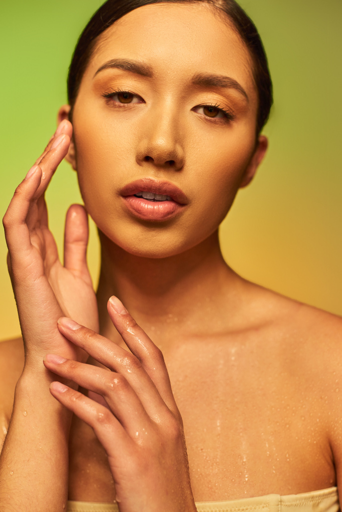 hidratáció, fiatal ázsiai nő csupasz vállak és nedves test pózol gradiens háttér, megható arc, nézi kamera, bőrápolási kampány, szépség modell, barna haj, ragyogó bőr  - Fotó, kép