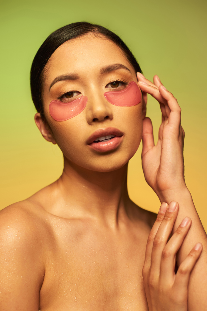 bonita e morena mulher asiática posando com manchas oculares em fundo verde, gradiente, beleza, desintoxicação da pele, tratamento facial, ombros nus, rotina de cuidados com a pele, pele brilhante, retrato  - Foto, Imagem
