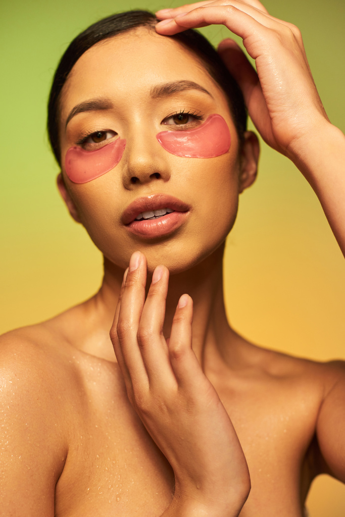 mooi en brunette aziatische vrouw poseren met ooglapjes op groene achtergrond, gradiënt, schoonheid, detox huid, gezichtsbehandeling, kale schouders, huidverzorging routine, gloeiende huid, portret  - Foto, afbeelding