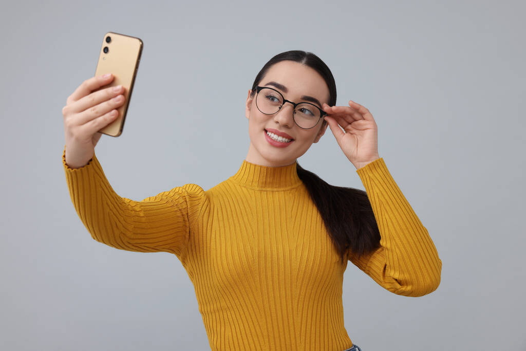 Sorrindo jovem mulher tomando selfie com smartphone no fundo cinza - Foto, Imagem